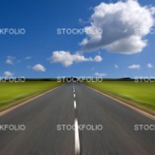 Rural road stretching out into the distance with motion blur under a big expanse of blue sky