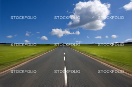 Rural road stretching out into the distance with motion blur under a big expanse of blue sky