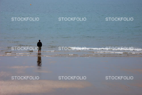 Solitary man wearing shorts standing on the edge of a beach looking out to sea