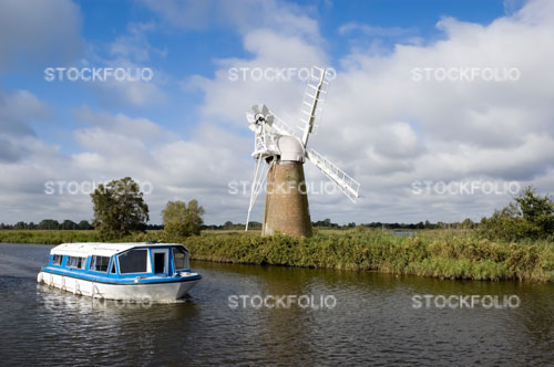 A boat passing Turf Fen windpump on the River Ant, Norfolk Broads